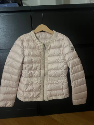 Ljusrosa dunjacka från Moncler - Säljer en ljusrosa dunjacka från Moncler med quiltad design och rund krage. Jackan har snygga ribbade detaljer vid krage, dragkedja och fickor samt Moncler-logga på ärmen. Stängs med dragkedja framtill och har två fickor. Jackan är 10/10 skick och är knappt använd. 