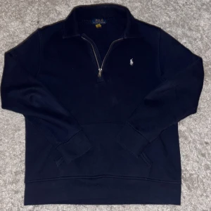 Mörkblå half zip tröja Polo Ralph Lauren - Säljer en mörkblå långärmad tröja från Polo Ralph Lauren med half zip och klassisk krage. Tröjan har ett broderat vitt Polo-logo på bröstet och är tillverkad i mjuk bomull med fleece på insidan. Perfekt för chill dagar och snygg till jeans.