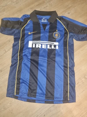 Nike Inter Milan Adriano tröja L - Säljer en Inter Milan matchtröja från Nike i storlek L med Adriano och nummer 28 på ryggen. Tröjan har klassiska blå och svarta ränder, gul Nike-logga och Pirelli-tryck på bröstet. Tillverkad i polyester med krage och snygga detaljer på sidorna.