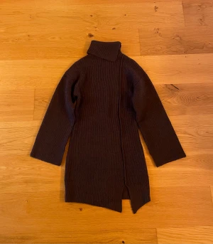 Brun stickad poloklänning NA-KD - Mysig brun stickad klänning från NA-KD i storlek XS. Klänningen har en asymmetrisk polokrage, lång ärm och en slits nertill. 