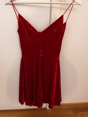 Röd sammetsklänning med rosetter - Supersöt röd kortklänning i mjuk sammet med tunna axelband och v-ringning. Baksidan har två stora rosetter som ger en extra wow-effekt. Perfekt för dig som vill sticka ut och känna dig extra fin.   Den är i lika bra skick som när jag köpte den, då den knappt är använd, max någon enstaka gång bara. (Minns tyvärr inte vart jag köpte den, därför står det inget märke i beskrivningen). 
