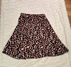 Leopardmönstrad kjol från V&L Firenze - Säljer en snygg leopardmönstrad kjol från V&L Firenze i djurmönstrat svart, orange och beige. Kjolen har resår i midjan och är i en luftig, lätt viskos som ger skön rörelse. Passformen är normal och kjolen är i en klassisk kort längd. Perfekt för dig som gillar djurmönster och vill sticka ut.