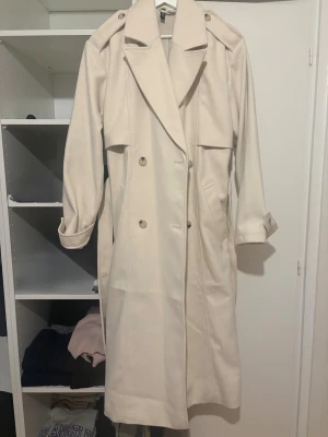 Beige trenchcoat från H&M  - Snygg beige trenchcoat från H&M i storlek S. Jackan har dubbelknäppning, bred krage och axelklaffar. Långa ärmar med knäppning vid mudden och två sidofickor. Är helt ny ej använd!