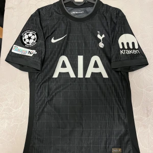 Tottenham Hotspur svart matchtröja - Säljer en svart Tottenham Hotspur player edition matchtröja från Nike med bergvall 15 på ryggen. Tröjan har UEFA Europa League 2025 Winners-märke och Foundation-patch på ärmen. Materialet är lätt polyester med diskret rutmönster och Dri-Fit ADV-teknologi.