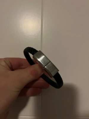 Svart flätad USB-laddningsarmband - Snyggt svart armband med flätad design och metallspänne som döljer en USB- och Lightning-kontakt. Perfekt för dig som vill ha laddningskabel nära till hands utan att kompromissa med stilen. Armbandet gör din outfit komplett! Hör av dig vid frågor✨🤩
