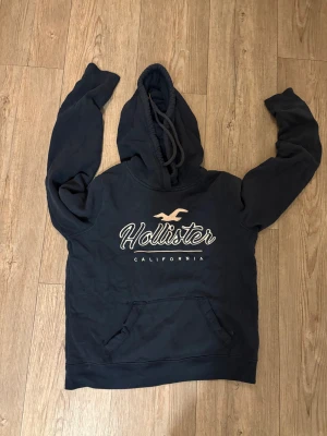 Hollister hoodie  - Säljer hollister hoodie mörkblå med påsytt tryck  och snörning. 