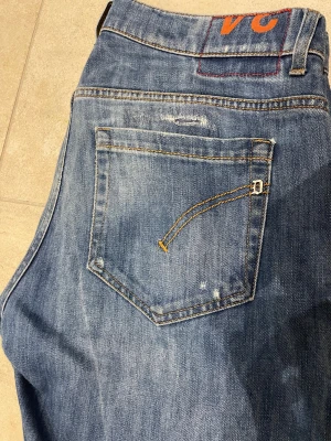 Blå  jeans från dondup - Säljer ett par blå slim jeans från dondup i storlek 34. Jeansen har slitna detaljer och hål framtill för en riktigt edgy look. Klassisk femficksmodell med kontrastsömmar och normal midja. Perfekta för dig som gillar streetstyle. Jeans sitter som ett par 33/31