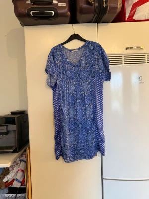 Blå mönstrad Odd Molly klänning - Supersöt kortklänning i blått med blommigt och geometriskt mönster. Klänningen har v-ringning, korta ärmar och är gjord i mjuk bomull. Perfekt för dig som gillar boho-vibe och vill ha något som sticker ut med coola detaljer. Från märket Odd Molly. Storlek 2 som enligt deras storleksguide motsvarar en M. Mycket fint skick, jag hittar inga synliga anmärkningar eller defekter.  