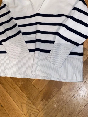 Vit och marinblå randig stickad tröja Zara - Säljer en vit stickad tröja från Zara i storlek L med marinblå horisontella ränder. Tröjan har breda ribbade muddar vid ärmslut och nederkant, samt en snygg v-ringad krage. Perfekt för dig som gillar klassisk och chill stil.
