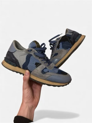 Valentino Garavani Rockrunner sneakers - Säljer ett par Valentino Garavani Rockrunner sneakers i blå, grå och svart camouflage. Skorna har snörning, rund tå och platt sula. Materialmix av mocka, mesh och skinn med coola detaljer och klassisk logga på plösen. Perfekt för dig som gillar exklusiva sneakers med unik design. Size 40 passar 41 tillkommer dustbag - extra snören