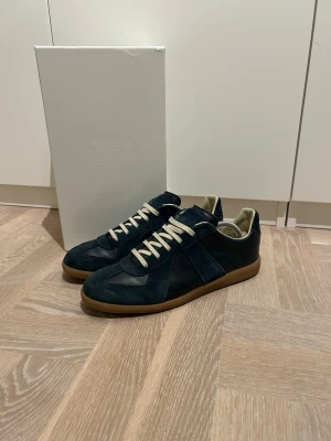 Mörkblå sneakers från Maison Margiela - Maison Margiela sneakers i mörkblå mocka och skinn med beige snörning och gummisula. Säljer pga är sugen på annat, använda ett par gånger i skolan. Pris kan diskuteras vid snabb affär😁