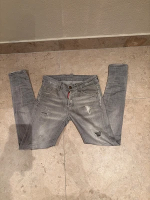 Gråa jeans från Dsquared2 - Säljer ett par gråa jeans från Dsquared2 med coola slitningar och färgstänk. Jeansen har klassisk femficksdesign och ett unikt Dsquared2-märke baktill i gult och svart. Jätte bra skick! Fråga hjärna vid funderingar