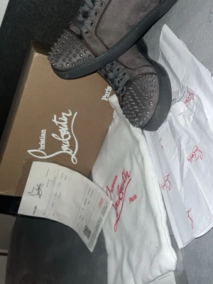 Christian Louboutin svarta sneakers med nitar - Säljer ett par svarta sneakers från Christian Louboutin med coola nitar på tån och klassisk röd sula. Skorna är gjorda i mocka och har snörning framtill. Kommer med originalkartong, dustbag och papper. Perfekt för dig som gillar edgy designerstil. Mockan kommer i super skick men nitarna börja missfärga sig, ingenting man ser!