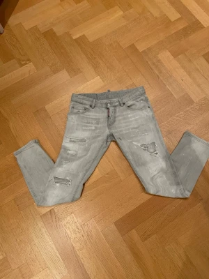 Grå slitna jeans från Dsquared2 - Snygga grå jeans från Dsquared2 med slitningar och hål på framsidan för en cool look. Modellen har, bälteshällor och klassisk knapp- och dragkedja. Materialet är 98% bomull och 2% elastan vilket gör dem bekväma och stretchiga.