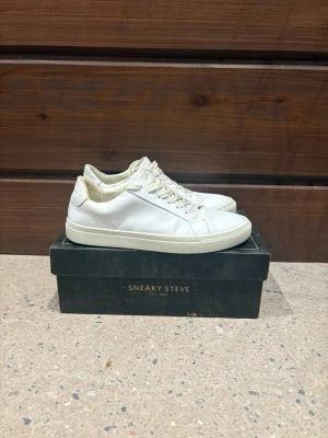Sneaky Steve vita skinnsneakers - Fräscha vita sneakers från Sneaky Steve i storlek 43. Skorna är tillverkade i slätt skinn med rund tå, snörning och platt sula. Klassisk och stilren design med diskret logga på plösen. Perfekta för dig som gillar minimalistisk stil. Allt på bild tillkommer. Pris är diskuterbart!