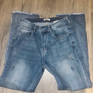 Blå skinny jeans med pärldetaljer Zac & Zoe - Snygga ljusblå skinny jeans från Zac & Zoe i storlek S/36. Jeansen har coola pärldetaljer med måne och stjärnor på benen samt råa, fransiga benslut. Materialet är stretchigt med 98% bomull och 2% elastan för skön passform. Defekt: hål på byxbenet längst ner.