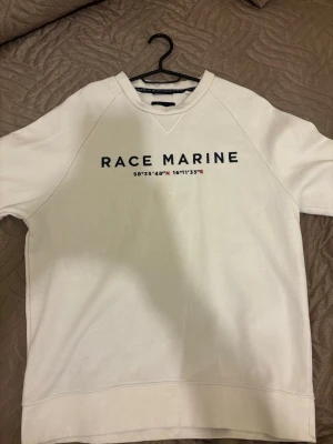 Vit sweatshirt från Race Marine - Säljer en stilren vit sweatshirt från Race Marine med tryck i svart och röda detaljer på bröstet. Tröjan har rund halsringning och korta ärmar, perfekt för en avslappnad look. Tillverkad i mjuk bomull för skön komfort.
