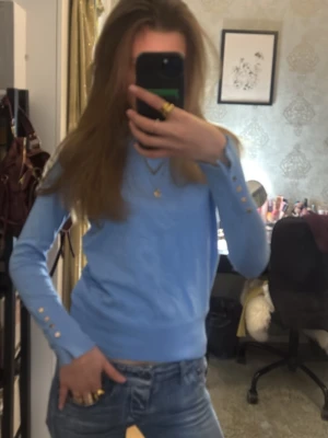 Ljusblå långärmad tröja med guldknappar - Snygg ljusblå långärmad tröja med rund hals och dekorativa guldknappar vid ärmsluten🥰🩵💛