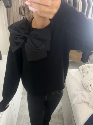 Svart stickad tröja med stor rosett - Säljer en svart stickad tröja med en riktigt stor rosett på axeln. 
