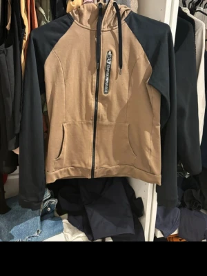 Emporio Armani Zip Hoodie – Size S - Selling an original Emporio Armani zip-up hoodie, purchased from JD Sports. In very good condition and well taken care of.  Brand: Emporio Armani Size: S Condition: Very good Color: Beige/brown body with black sleeves Full zip closure and hood with adjustable drawstrings Front pockets Authentic item (bought at JD Sports)  Modern, clean design with a premium feel. Perfect for everyday wear or a stylish streetwear look.  From a smoke-free home. Fast shipping