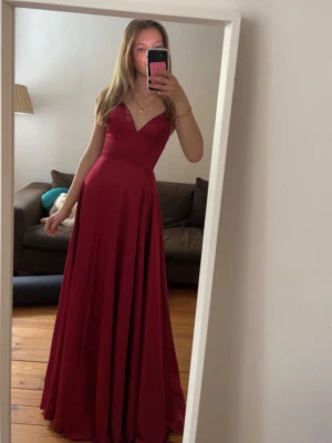 Vinröd balklänning klänning med snörning - Säljer en elegant vinröd balklänning med v-ringad front och smala axelband. Klänningen har en snygg snörning i ryggen som ger en öppen och unik look. Materialet är mjukt och faller fint, perfekt för bal eller student. Nypris 3300. Från ivory fields med några fläckar längst ner