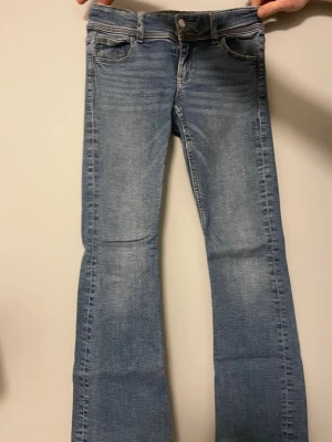 Blå bootcut jeans med fickdetaljer från gina  - Snygga blå bootcut jeans från Gina tricot den gamla modellen med klassisk femficksdesign och dekorativa knappar på bakfickorna. Jeansen har en ljus tvätt och raka sömmar. Jeansen är 93cm långa från midjan och 35cm breda vid midja till midja samt så är den 20 cm low waisted men blir dock mindre när man sätter på dem. Skriv till mig om ni har några frågor 🤗