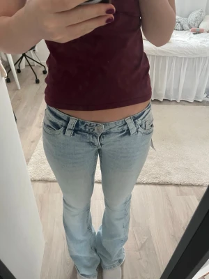 Ljusblå bootcut jeans låg midja från Gina  -  ett par ljusblå bootcut jeans med låg midja och ljus tvätt. Jeansen har rosa detaljer på bakfickorna. Jeansen är helt nya med prislapp kvar och har aldrig använts.  är från Gina tricot och passar mig som är 166