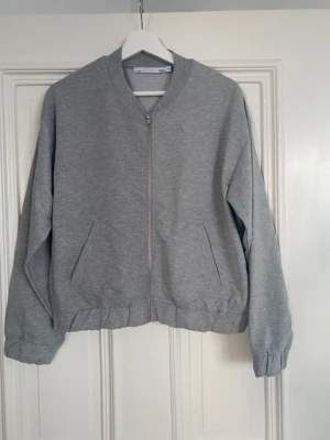 Grå bomberjacka från 157 - Säljer en enkel och clean grå bomberjacka från 157 med dragkedja framtill och två fickor. Jackan har ribbade muddar vid krage och ärmslut samt en relaxed passform. Perfekt till lager på lager och chill vardagsstil.