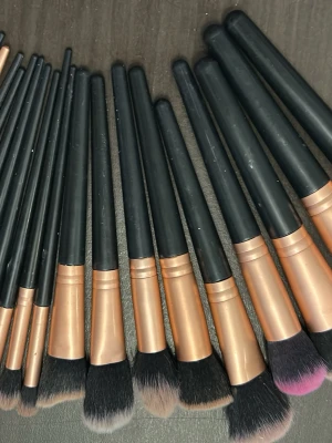 Set med sminkborstar i svart och koppar - Säljer ett stort set med sminkborstar i olika storlekar och former. Handtagen är svarta med kopparfärgade detaljer och borstarna har mjuka syntetiska strån i svart, vitt och lite rosa. Perfekt för foundation, contour, ögonskugga och detaljerad applicering.