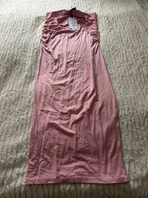 Rosa långkjol med rynkade detaljer - Superskön långkjol i mjukt rosa tyg Kjolen har rynkade detaljer vid midjan som ger en snygg och trendig look. Perfekt för dig som gillar en enkel men ändå stylish vibe.