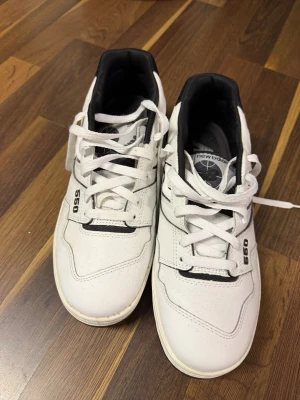 New Balance 550 vita sneakers - Säljer ett par New Balance 550 sneakers i vitt med svarta detaljer. Klassisk retrostil med snörning, rund tå och platt sula. Ovandelen är i skinn och syntet, insidan är svart och de har tydlig 550-märkning på sidan. Perfekta för dig som gillar streetwear och sportig look. Använda 1 gång