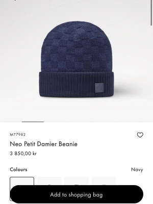 Mörkblå stickad huvudbodnad Louis Vuitton - Säljer en mörkblå stickad huvudbodnad från Louis Vuitton med diskret rutmönster och en snygg patch med logga framtill. Huvudbodnaden är tillverkad i mjukt material och har en klassisk, stilren look som passar perfekt till lager-på-lager outfits.