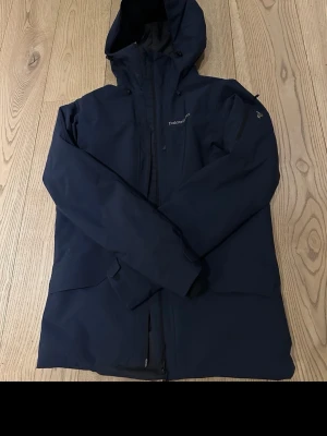 Mörkblå vindjacka Peak Performance - Säljer en mörkblå vindjacka från Peak Performance med huva och dragkedja framtill. Jackan har en clean look, diskret logga på bröstet och praktiska fickor. Perfekt för dig som vill ha en stilren och funktionell jacka till vardags. Plus skidor