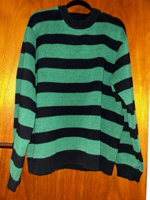 Randig grön och svart tröja Vaillent - Säljer en snygg randig tröja från Vaillent i grönt och svart. Tröjan har breda horisontella ränder, rund halsringning och ribbade muddar vid ärmslut och nederkant. Perfekt för dig som gillar en chill och stilren look.