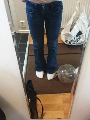 Blå bootcut jeans Gina Tricot 152 - Säljer ett par mörkblå bootcut jeans från Gina Tricot i storlek 152. Jeansen har klassisk femficksdesign, normal passform och lätt utsvängda ben. Materialet är jeans med slitna detaljer vid bensluten för en avslappnad look.
