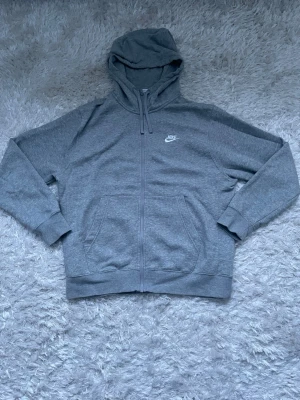 Nike grå zip-hoodie — storlek M, fint skick  -  Grå Nike hoodie med dragkedja i storlek M. Klassisk och stilren modell med liten vit Nike-logga på bröstet. Mjuk och bekväm insida, perfekt för vardag, skola eller träning. I fint skick.  Storlek M