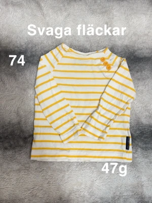 Randig långärmad topp Polarn O. Pyret - Vit och gul långärmad topp från Polarn O. Pyret med smala ränder och tre knappar på axeln. perfekt för lek och vardag. Klassisk och enkel design som passar till mycket.🌸 Svaga fläckar. Storlek 74