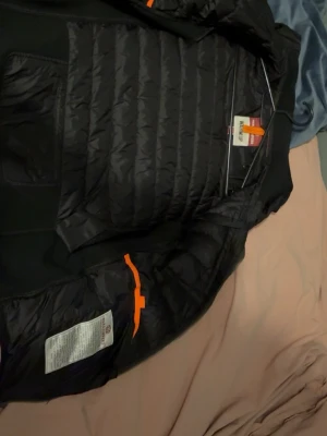 Svart pufferjacka Parajumpers S - Säljer en svart pufferjacka från Parajumpers i storlek S. Jackan har quiltad front i syntetmaterial, meshliknande ärmar och detaljer i gult. Klassisk patch på ärmen och dragkedja framtill. Perfekt för dig som vill ha en sportig och clean look. det ända felet är att inne fickorna är lite söndriga! men går att sy lätt 
