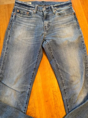 Levi's 511 blå jeans - Säljer ett par klassiska Levi's 511 jeans i ljusblå tvätt. Modellen har normal passform med något smalare ben, fem fickor och snygga slitningar fram och baktill. Perfekta för en avslappnad och stilren look. Vid frågor är det bara att skriva eller om priset inte passar!