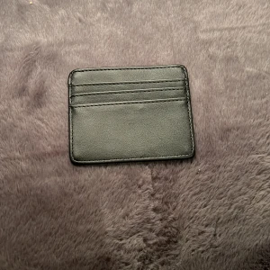 Jag säljer en plånbok enkel lätt få plats i fickor  - Minimalistiskt svart kortfodral i slätt skinn med plats för flera kort på båda sidor. Perfekt storlek för fickan och stilren design utan logga eller extra detaljer. Enkel och clean look för dig som gillar det klassiska.