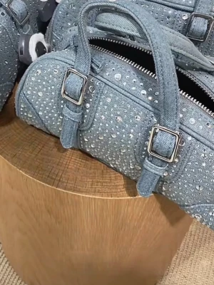 Blå handväska i denim med paljetter - Säljer en blå handväska i denim med glittriga paljetter över hela väskan. Väskan har två handtag, silverfärgade spännen och en dragkedja upptill. Priset går att diskutera 