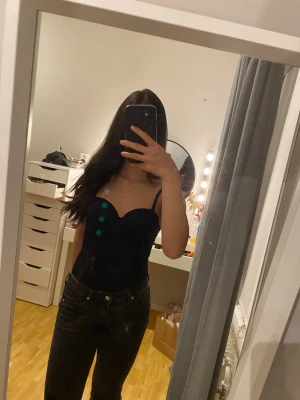 Svart body från H&M - Snygg svart body med smala axelband och formade kupor. Bodyn har en öppen rygg med spänne och är tillverkad i ett glansigt, stretchigt material som ger en tight passform. Perfekt att styla med jeans eller kjol för en trendig look. Banden går att ta av