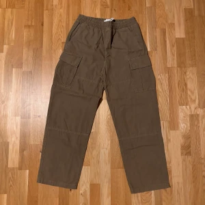 Gröna cargopants från Weekday - Säljer ett par gröna cargopants från Weekday med elastisk midja och snörning. Byxorna har stora sidofickor, raka ben och är gjorda i bomull. Perfekta för en chill och avslappnad stil.