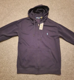 Polo kofta / polo rozpinane - Snygg mörkblå hoodie från Polo Ralph Lauren med dragkedja och huva med snörning. Den är I storlek M kan även passa S. Tillverkad i 100% mjuk bomull. OBS: färgen ser lite dåligare ut på bilden men inte i verkligheten. Vid snabbaffär kan priset diskuteras och även frakta vid det första tillfället.