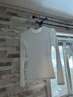 Vit långärmad topp från Zara - En stilren vit långärmad topp från Zara Modellen är figurnära med rund halsringning och passar perfekt till lager-på-lager eller som basplagg. Enkel och clean design som funkar till många olika looks.