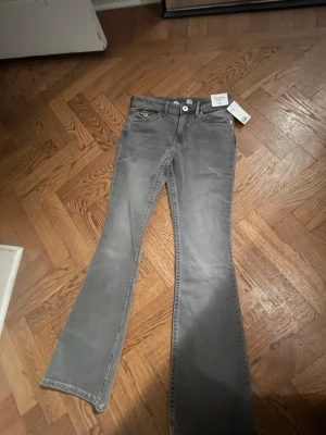 Grå bootcut jeans från H&M,har aldrig använt/helt nya. (164)13-14!  Säljer för att det var för långa! Pris kan diskuteras  - Snygga grå jeans från H&M med bootcut och flared ben. Jeansen har broderade bakfickor med små glittriga detaljer och knappar.