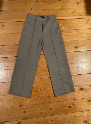 Kostymbyxor från Stockh LM - Snygga kostymbyxor från Stockh LM med raka ben och pressveck. Byxorna har hög midja, hällor för bälte och stängs med hake och dragkedja. Materialmix av lyocell, linne och bomull ger en skön känsla och stilren look.