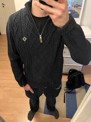 Mörkblå stickad tröja Morris half zip - Säljer en mörkblå stickad tröja från Morris med halv dragkedja och hög krage. Tröjan har ett snyggt kabelstickat mönster framtill och en broderad logga på bröstet. Perfekt för kyliga dagar och passar till jeans eller chinos.