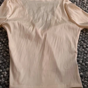 Ljusbeige omlottopp med knyt - Säljer en ljusbeige omlottopp med lång ärm och snygg knytning framtill. Toppen har v-ringad urringning och är gjord i ett mjukt, lätt material som ger en skön känsla. Perfekt att styla med jeans eller kjol för en trendig look. Köpte denna i Spanien så därav stämmer det inte att den är från Zara, den har inget specifikt varumärke 