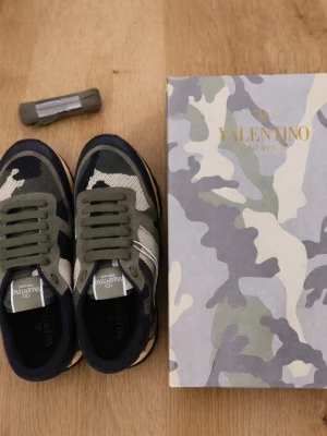 Valentino Rockrunner  - Säljer ett par Valentino Rockrunner sneakers i camouflage med olivgröna, beige och svarta toner. Skorna har snörning, mockadetaljer och coola nitar på hälen. Materialmix av mocka, skinn och textil ger en lyxig känsla. Perfekta för dig som vill sticka ut med stil